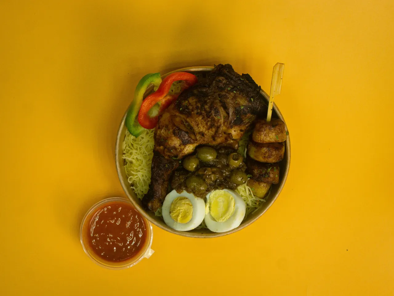 A bowl of grilled chicken with vermicelli, olives, boiled egg and plantain