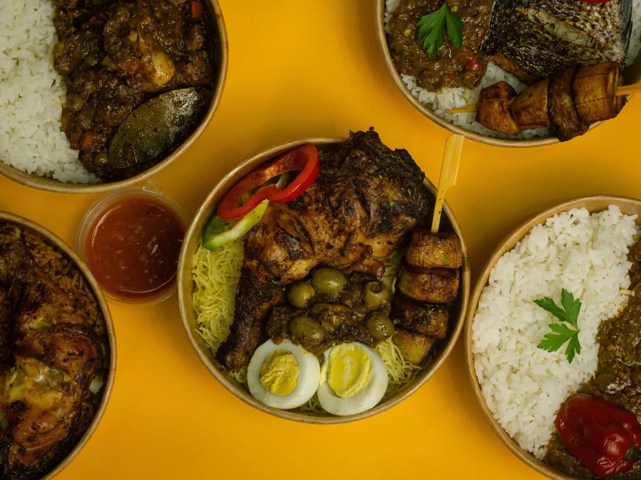Five bowls of Gambian dishes laid out together on a yellow table